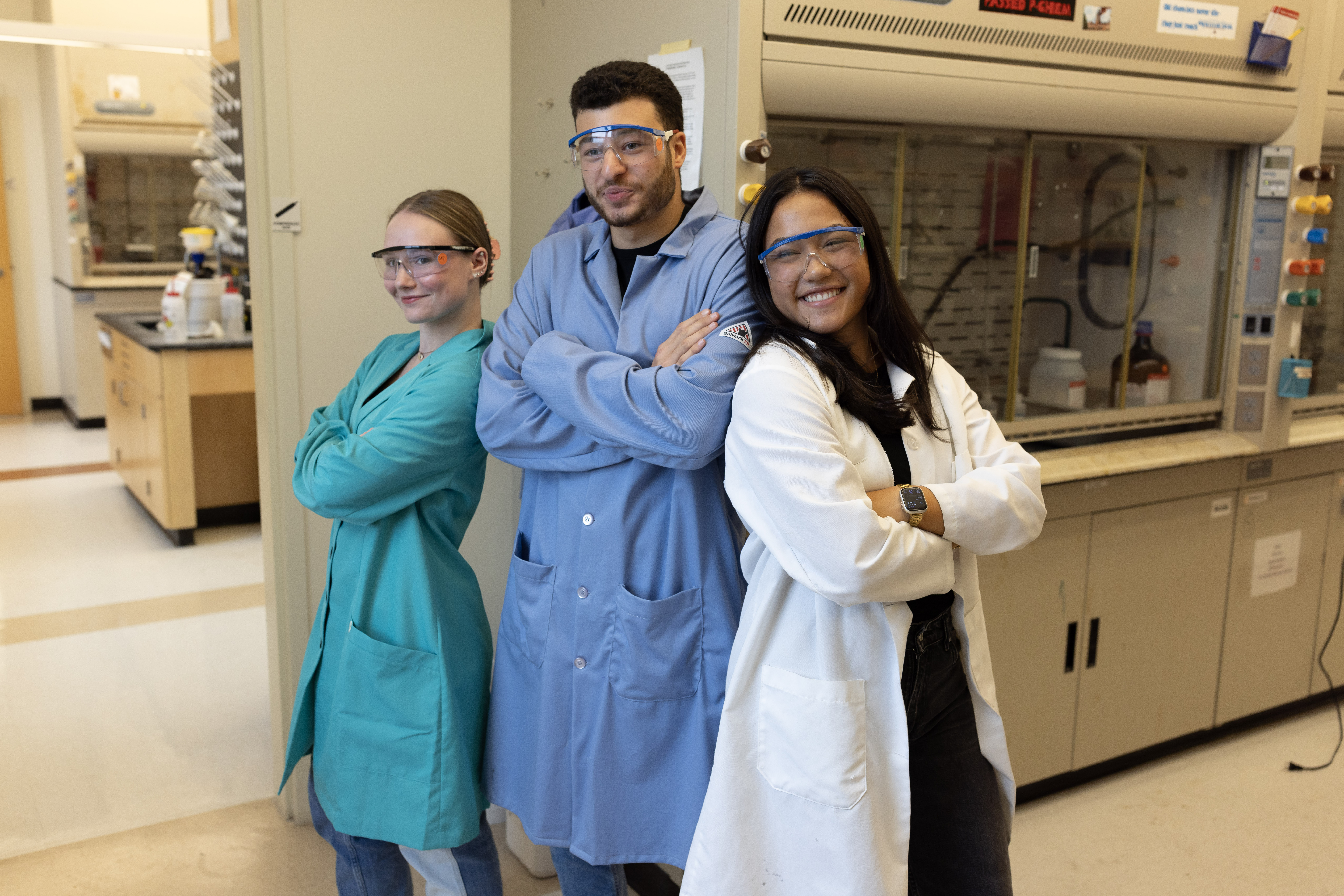 Three science students wearing lab coats pose back to back