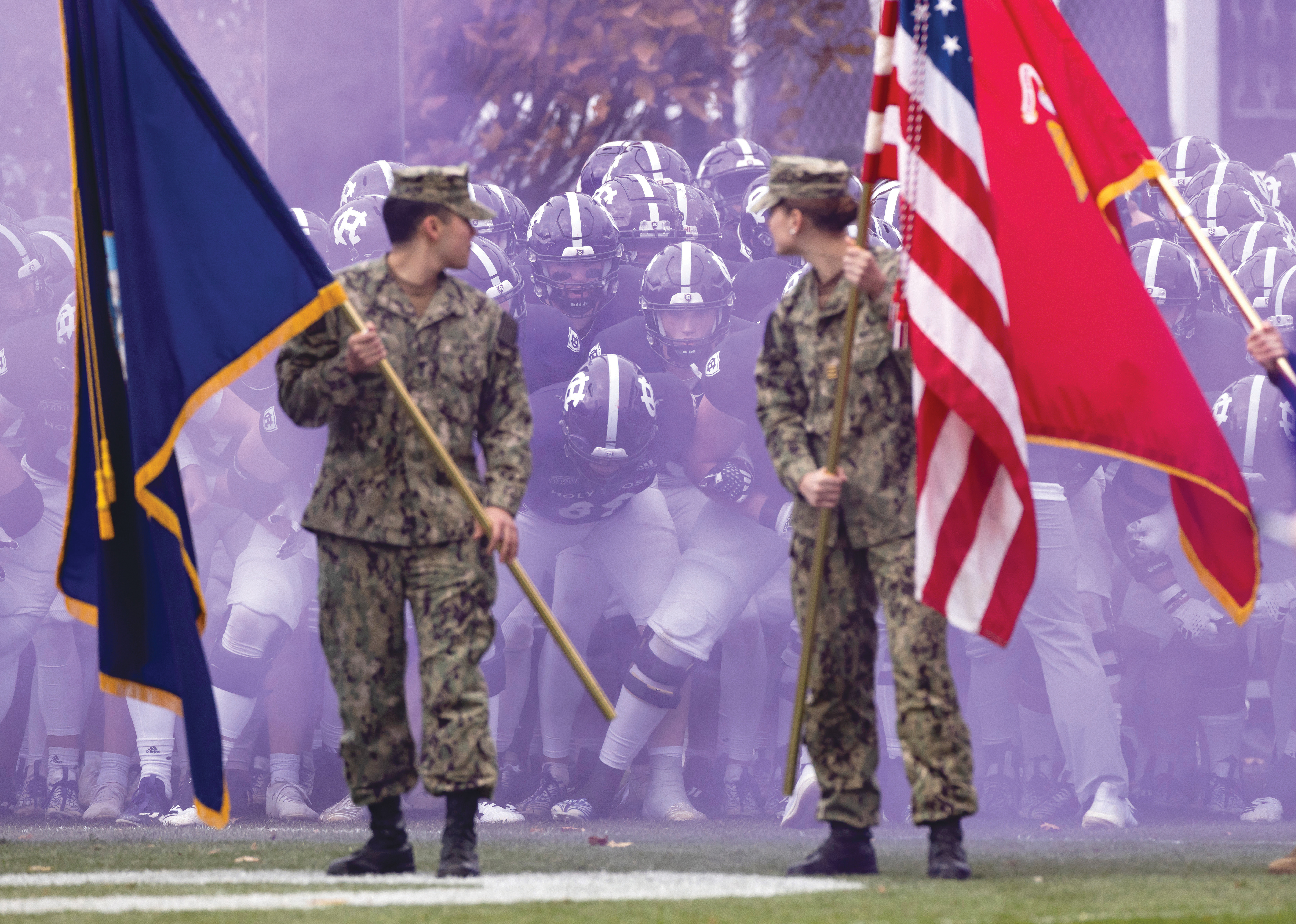 Football players ruin out on to the field behind a cloud of purple smoke