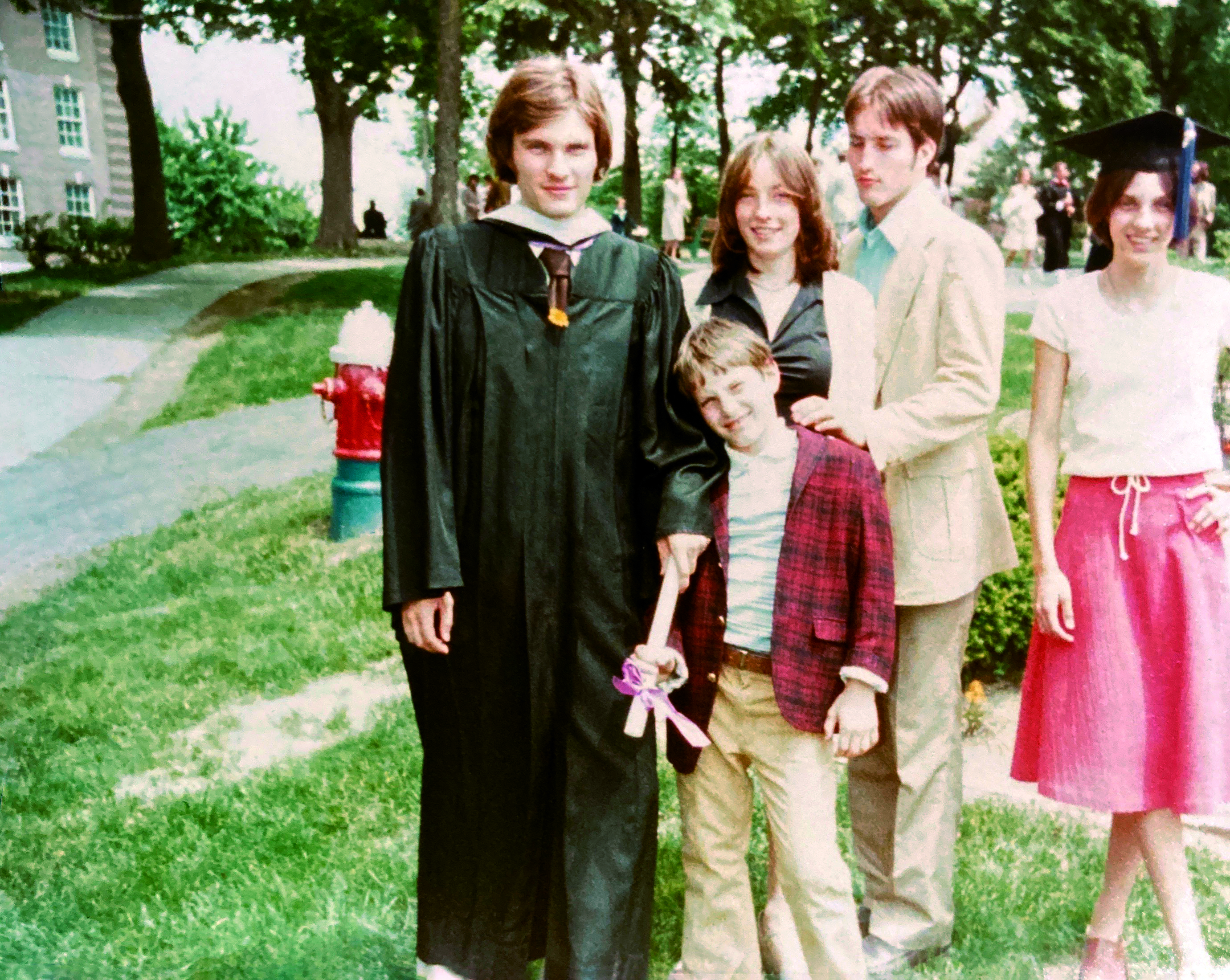 Man in graduation gown stands with four children