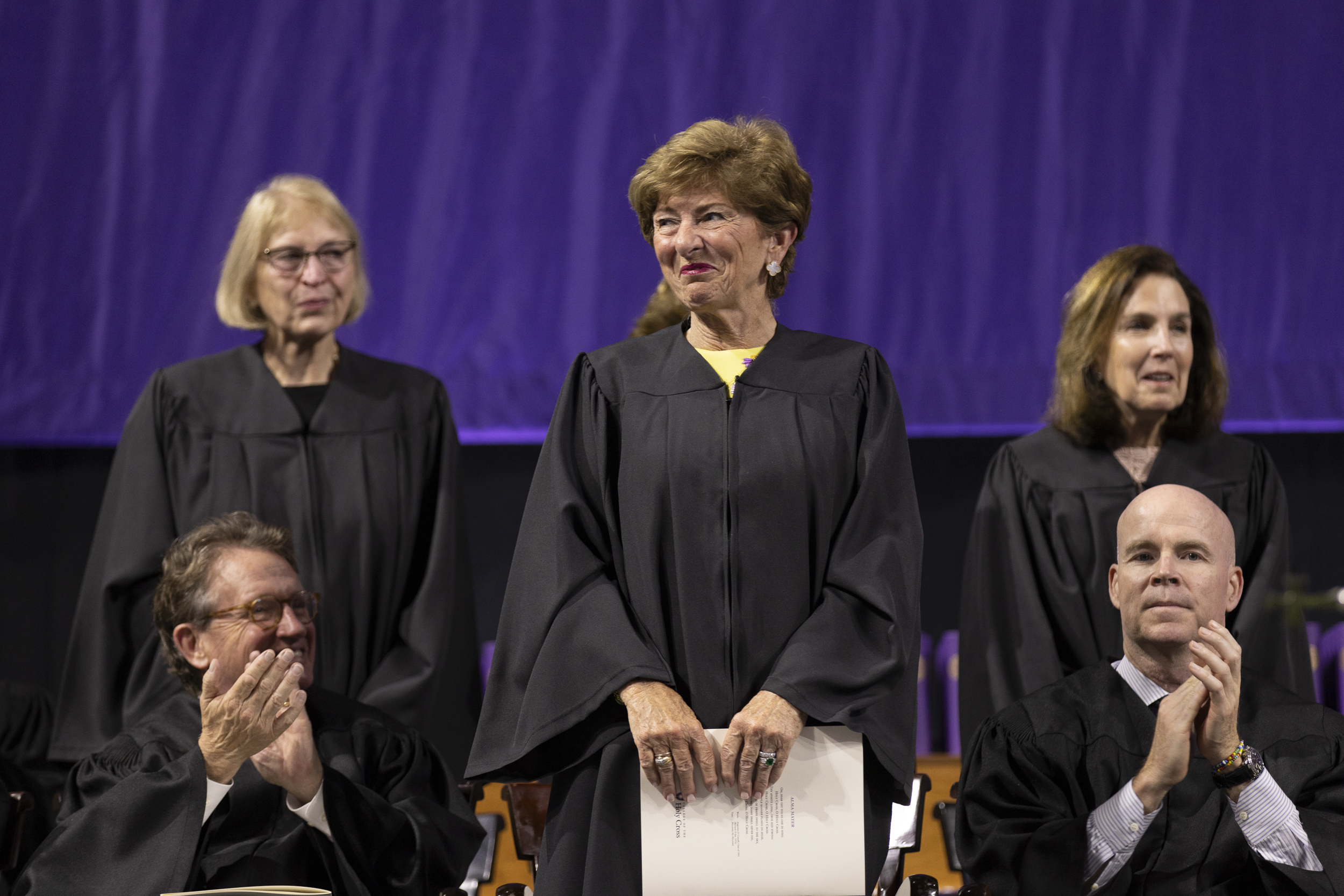 Three women dressed in black graduation robes stand during a commencement ceremony.