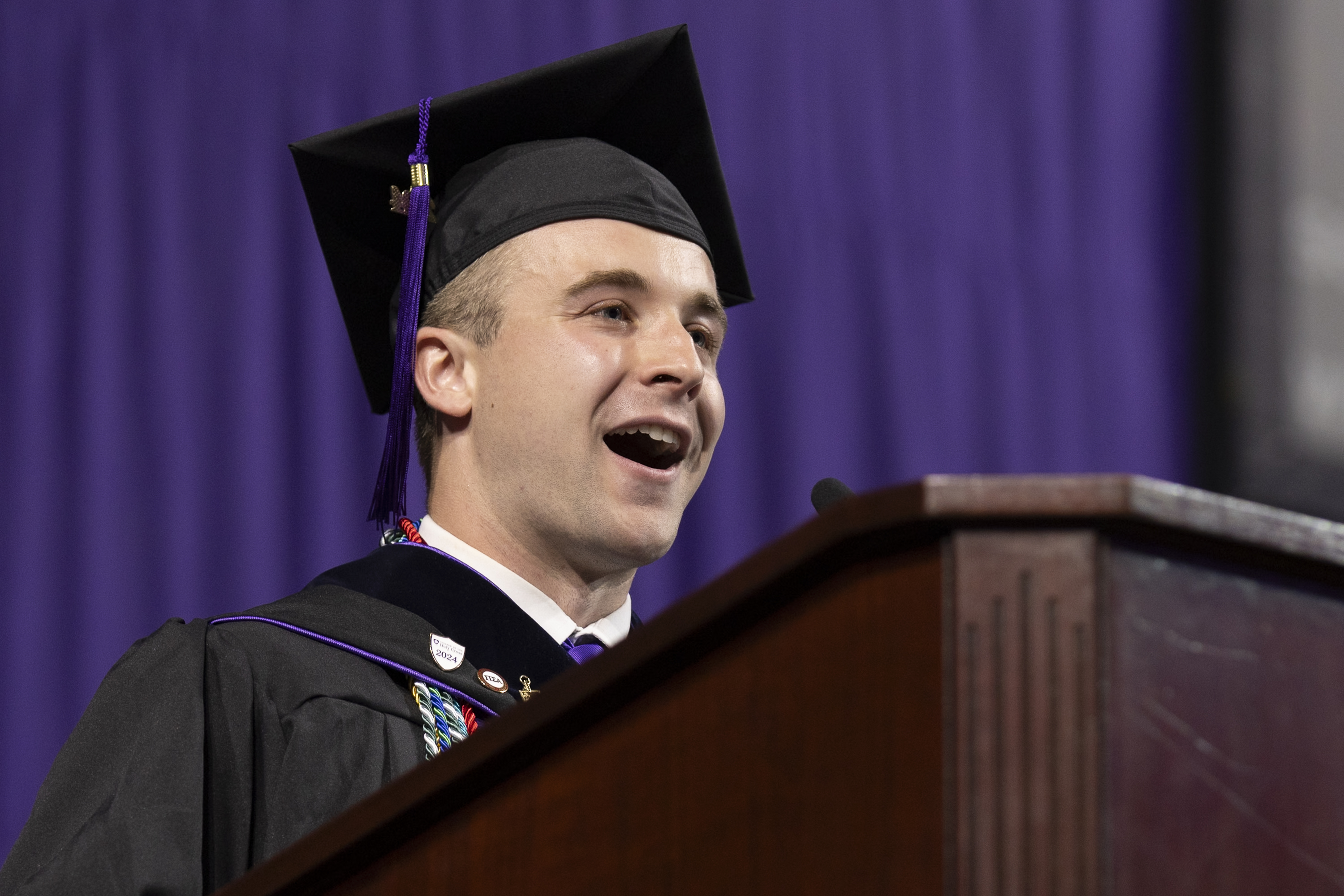 A male valedictorian smiles at his audience during his commencement address.