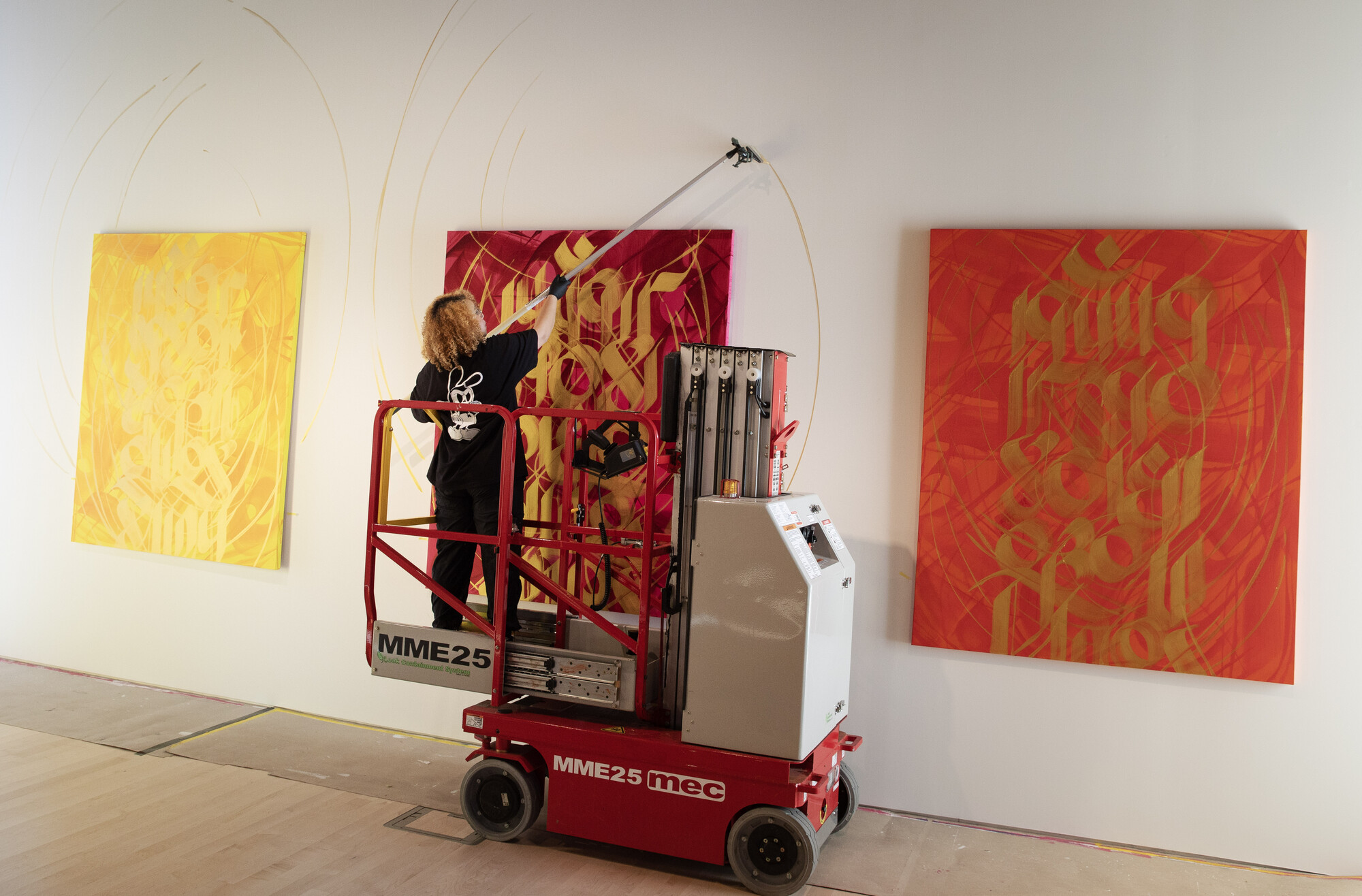 Artist Sneha Shrestha stands on scaffolding to install her paintings