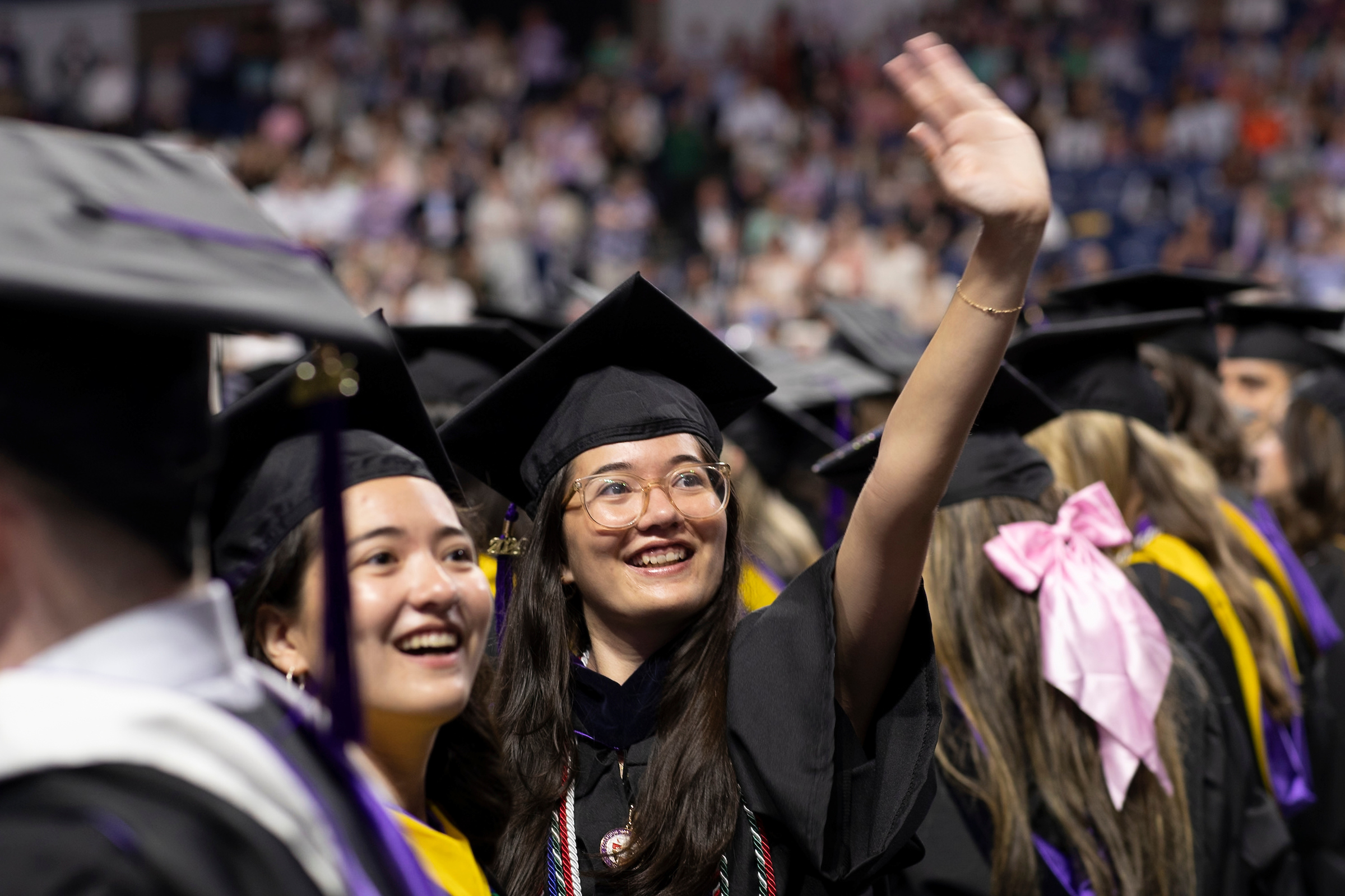 Women college graduate waving to family from the audience during commencement ceremony.