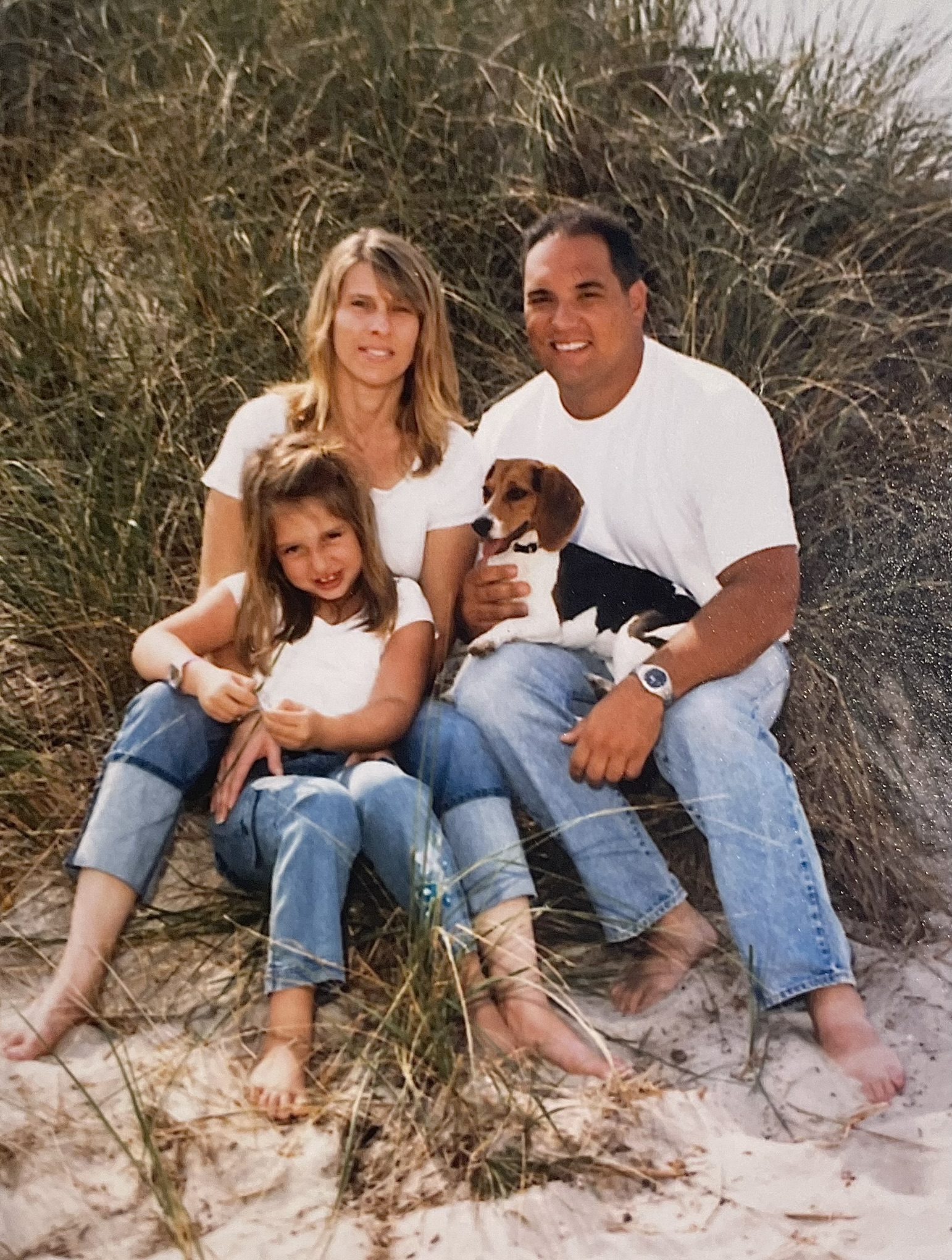 Young girl with her parents and dog sitting in sand dunes.