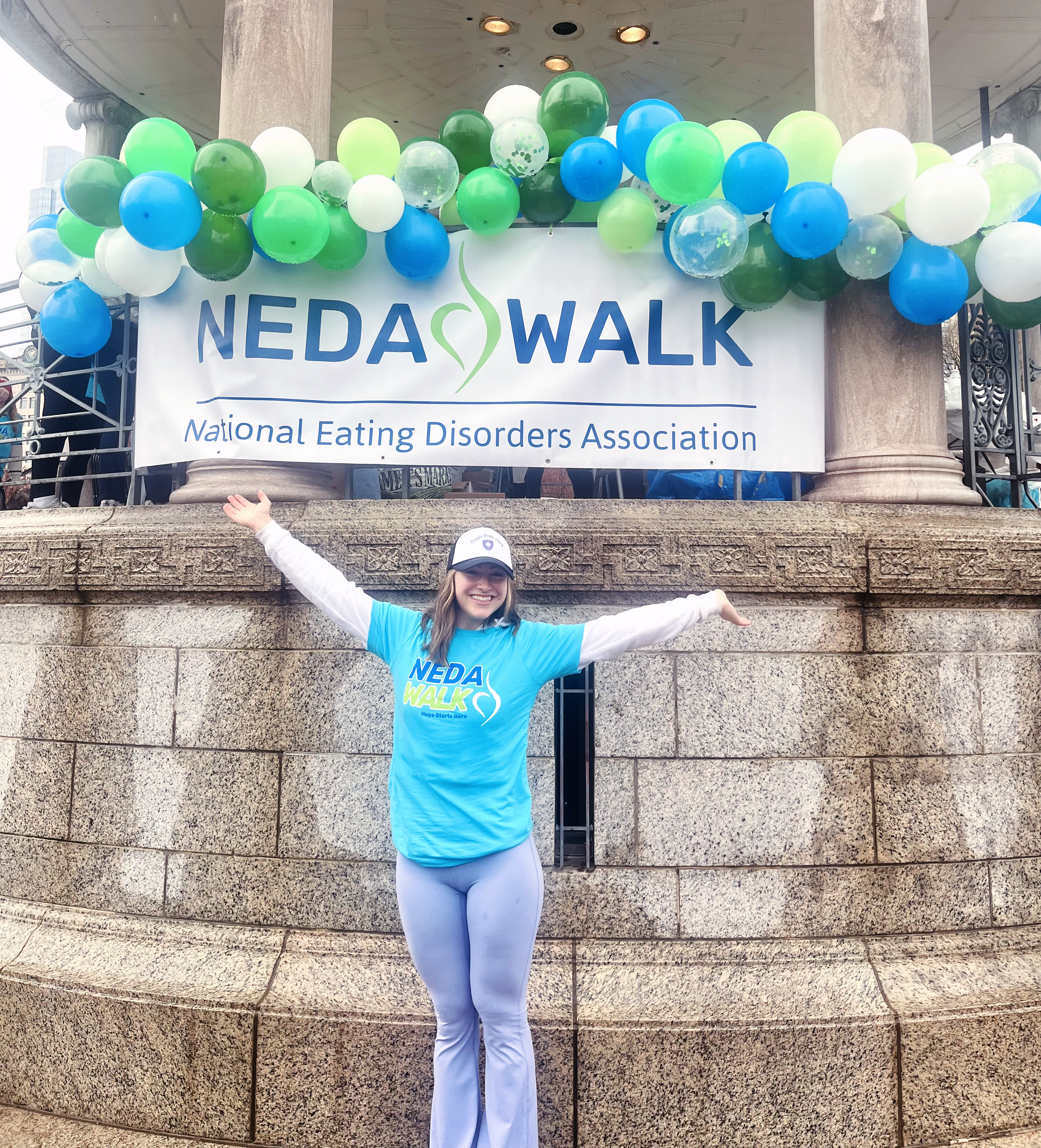 A young woman stands in front of a National Eating Disorders Association sign topped with balloons