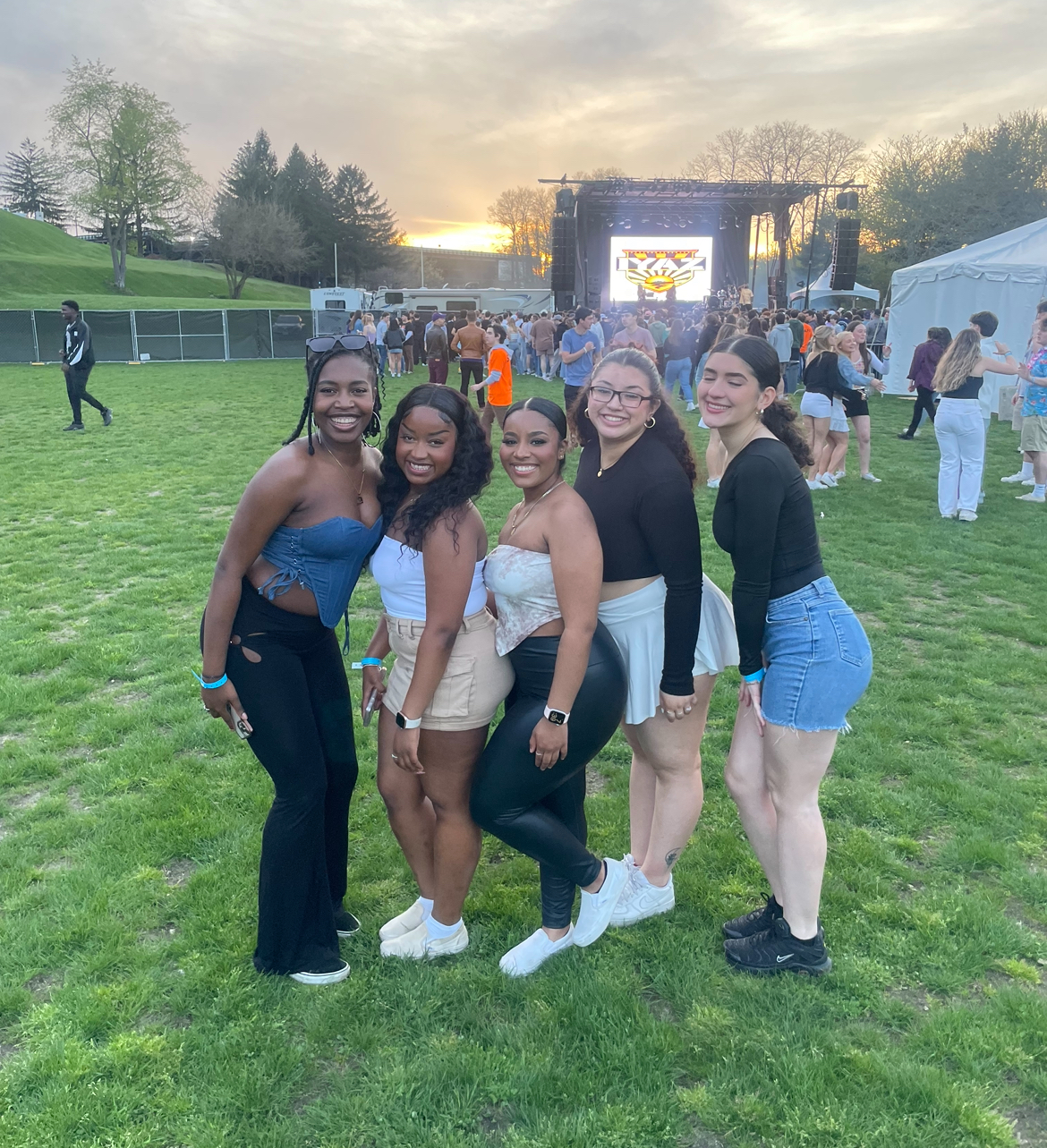 Five young woman posing for a photo with a concert stage behind them
