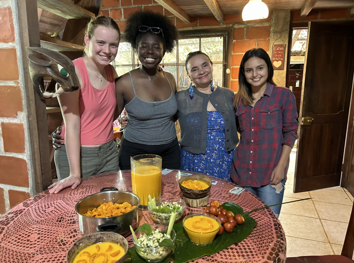 A group of young woman stand next to each other behind a table with plates of food