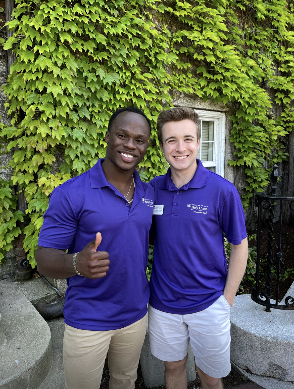 Two young men standing together in front of a wall of ivy