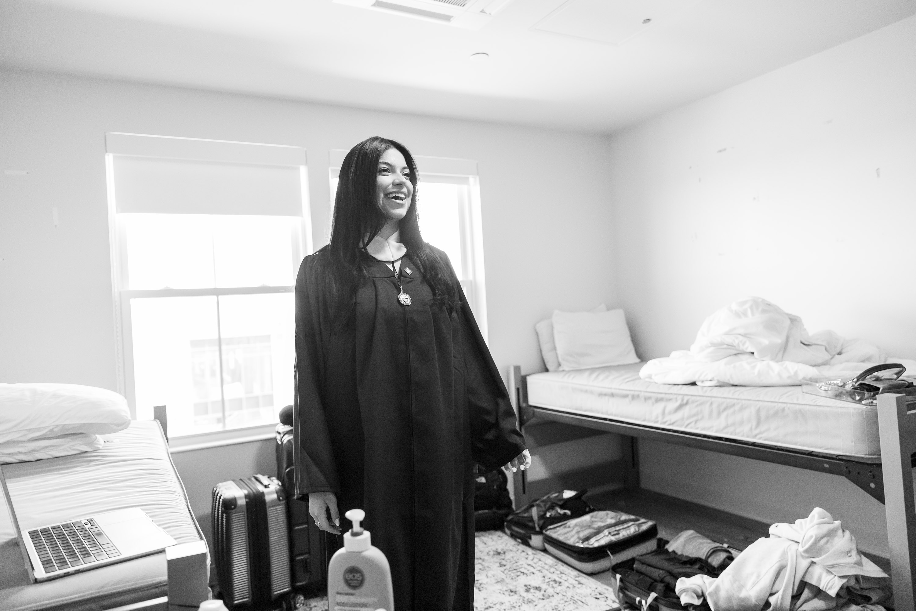 A woman looks at her reflection after putting on her graduation gown.