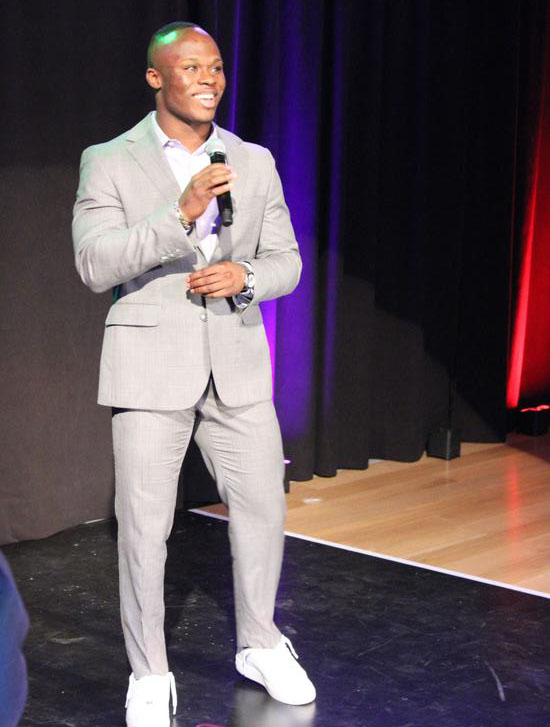 A young man in a light suite standing on a stage holding a microphone
