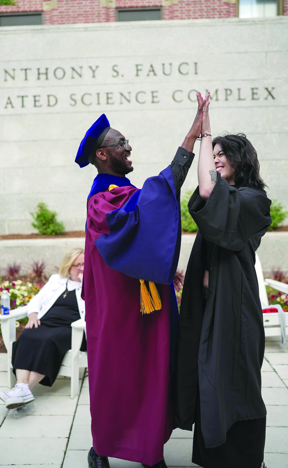 André Isaacs in commencement regalia high fiving a young woman, also in a cap and gown
