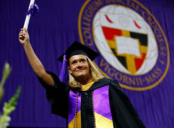 A student holds up their diploma while walking across stage.