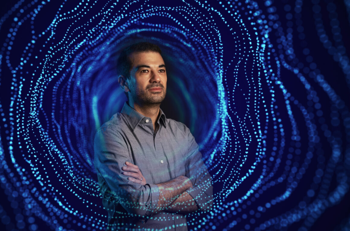 Male professor posing in front of blue background with arms folded.