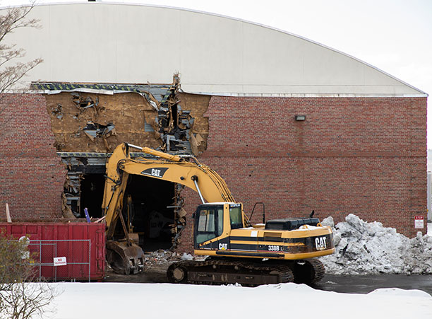 The side of the Field House with a large hole ripped into it, flanked by construction equipment