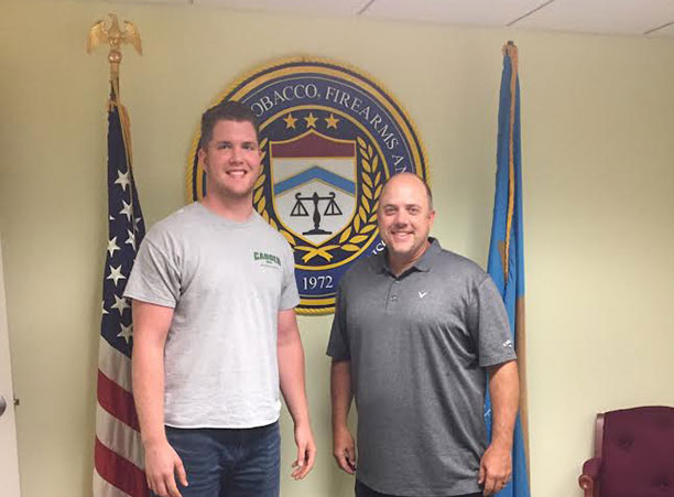 Two people stand in front of a sign for the Bureau of Alcohol, Tobacco, Firearms, &amp; Explosives