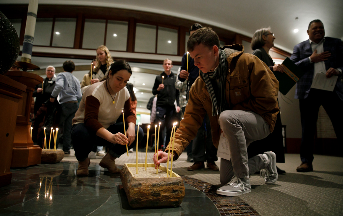A man and a woman place lit candles in a holder