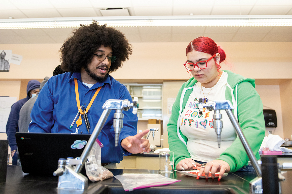 Gordon Burnett '12 IS talking through an experiment with a student in his Advanced Placement Chemistry class.