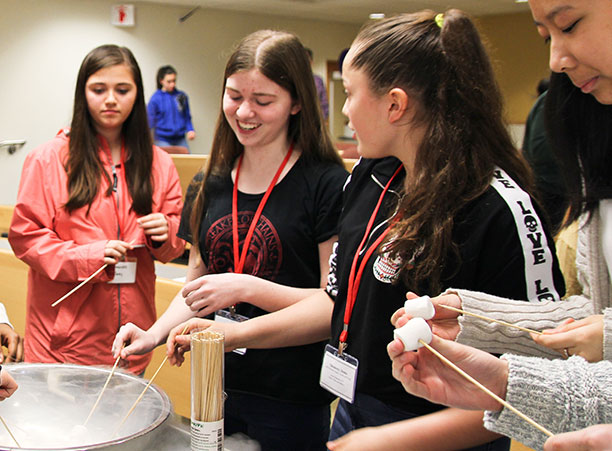 Students hold marshmallows on sticks in a bowl full of smoke