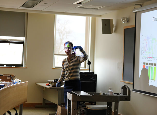 A professor wears safety goggles while holding a beaker of liquid