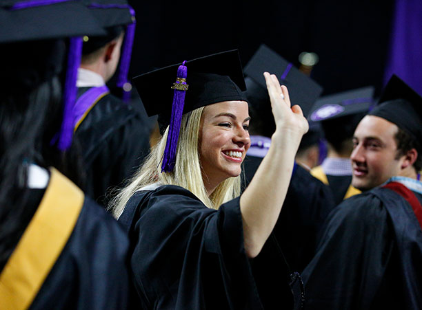 A student waves while processing into the DCU Center.