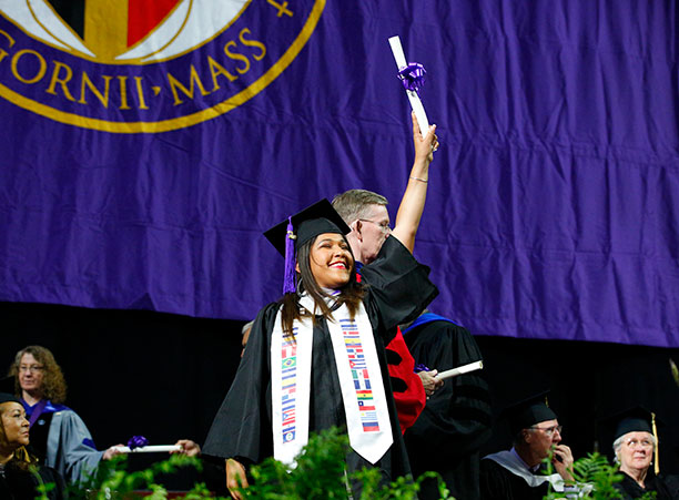 A student celebrates receiving their diploma on stage.