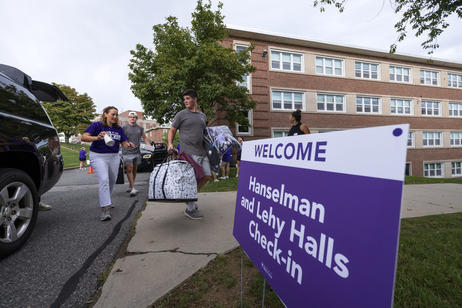 Students approaching a dorm with bags