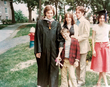 Man in graduation gown stands with four children