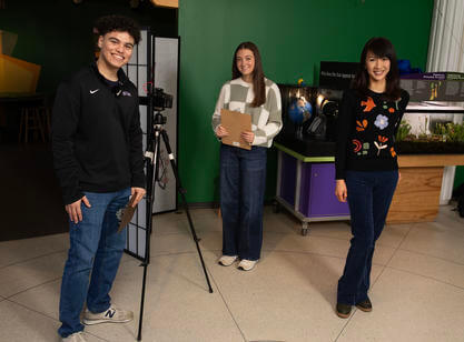 Two women and one man stand near a camera tripod in the middle of a science museum.