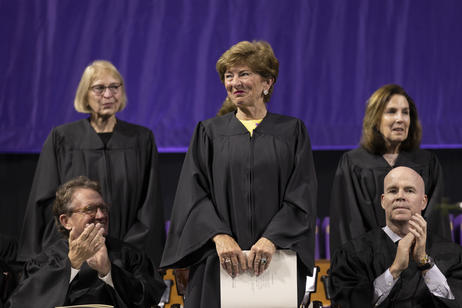 Three women dressed in black graduation robes stand during a commencement ceremony.