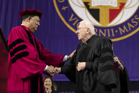 A male honorary degree recipient shakes a college president's hand during a commencement ceremony.