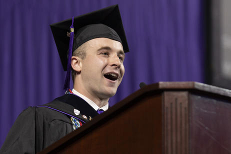 A male valedictorian smiles at his audience during his commencement address.