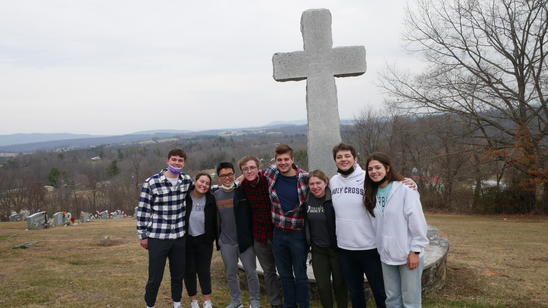 A group of young people stand by a large concrete cross