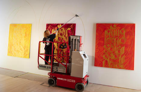 Artist Sneha Shrestha stands on scaffolding to install her paintings