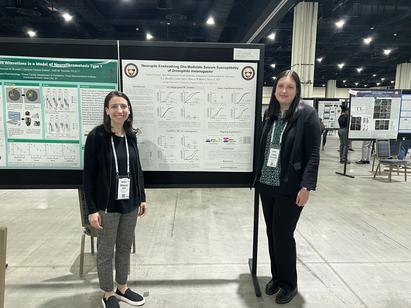 Professor and student at a conference poster presentation standing in front of a large board.