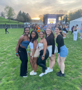 Five young woman posing for a photo with a concert stage behind them
