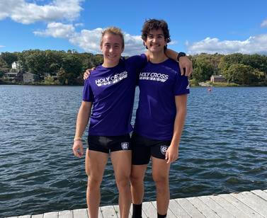 Two young men from the Holy Cross rowing team smile with arms around each other's shoulders in front of a body of water
