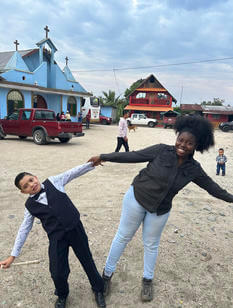 A young woman and a child hold hands while leaning away from each other