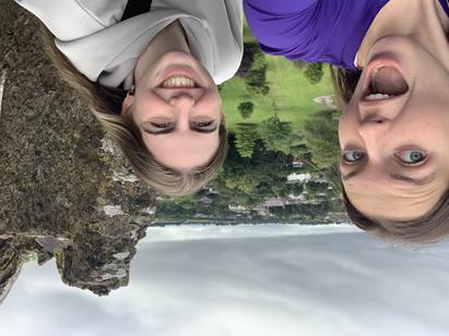 Two young women standing atop the rubble of a castle and a valley behind them