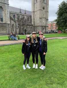 Three young women in matching sweatshirts standing in front of a brick church