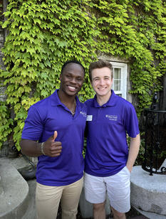 Two young men standing together in front of a wall of ivy