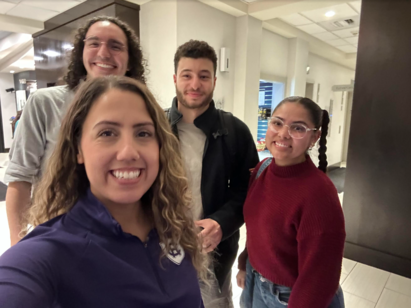 Three students and an admission director pose for a selfie in a hallway