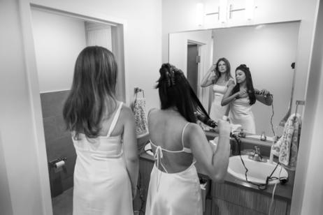 Two woman adjust their hair while looking into a mirror.