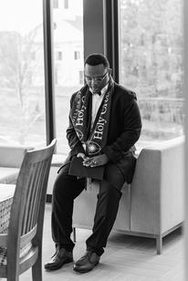 A young man in a suit leans up again a chair