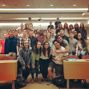 A group of people squeezing together for a photo in a college classroom