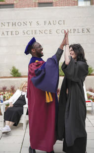 André Isaacs in commencement regalia high fiving a young woman, also in a cap and gown