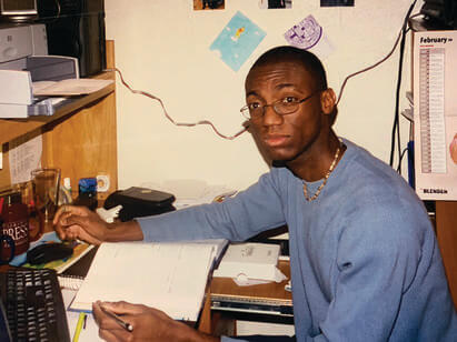 André Isaacs sitting at a desk in a resident hall with a book in front of him