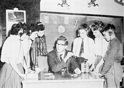 Black and white photo of students standing around a teacher