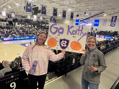 Two women holding a "Go Kaitlyn" sign in a basketball arena