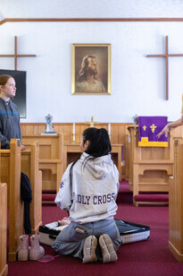 Student kneeling next to suitcase in church