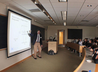 Gus Caffrey points to a slide presentation in front of a physics class.